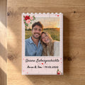 Bausteinbild mit Foto im Rahmen Liebe liegt auf einem Eichentisch, Draufsicht: Paarfoto farbig auf weißen Bausteinen mit Rosen, Überschrift und Namen in Handschrift