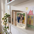 Bausteinbild im Rahmen Familie mit Familienfoto steht im Regal neben Büchern und einer Kinderzeichnung