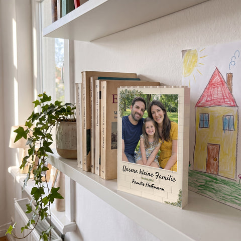 Bausteinbild im Rahmen Familie mit Familienfoto steht im Regal neben Büchern und einer Kinderzeichnung