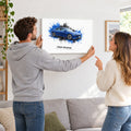 Paar hängt eine personalisierte Leinwand mit blauem E-Auto im Wohnzimmer auf