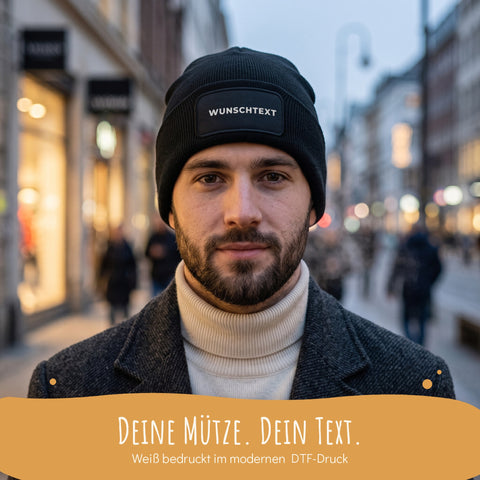 Mann in der Stadt trägt ein schwarzes Beanie mit Wunschtext, Deine Mütze, Dein Text