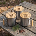 Drei Edelstahlbecher mit gelasertem Bambusdeckel und Namen auf einem Holztisch