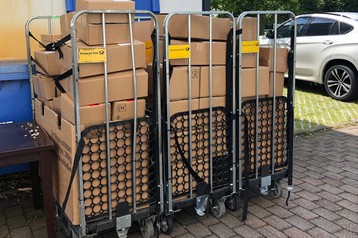 Archivbild vom Mai 2019: drei Rollwagen der Deutschen Post voller Pakete vor der Tür an der Kelvinstraße