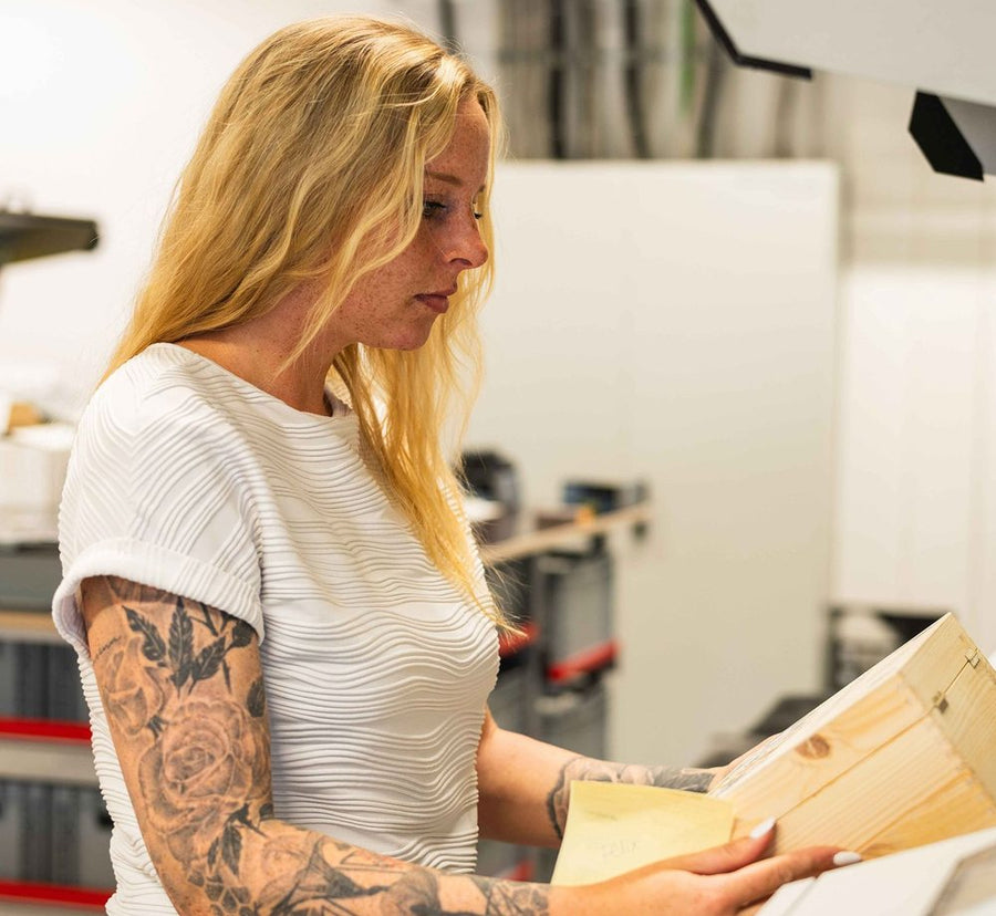 Mitarbeiterin in der Produktion legt eine Holzkiste in die Lasermaschine