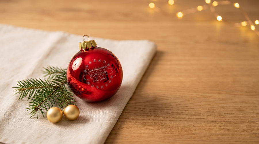 Gravierte rote Weihnachtskugel mit Tannenzweig auf einem Holztisch