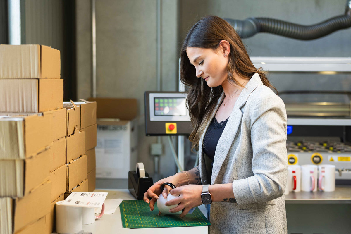 Mitarbeiterin in der Produktion bereitet Tassen für den Druck vor