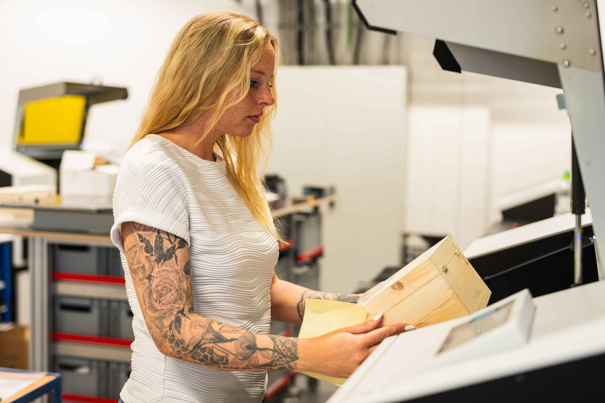 Mitarbeiterin in der Produktion legt eine Holzkiste in die Maschine